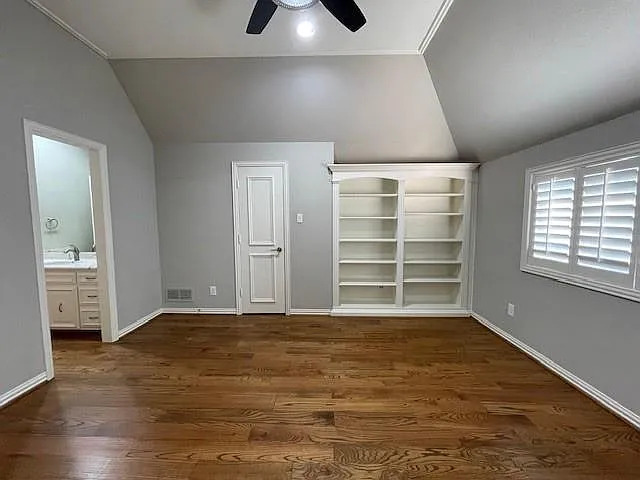 Unfurnished bedroom with lofted ceiling, dark wood finished floors, ensuite bathroom, and ceiling fan
