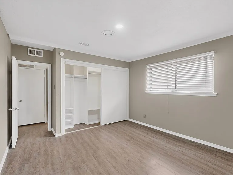 A bedroom featuring hardwood floors, a built-in closet and a wide window