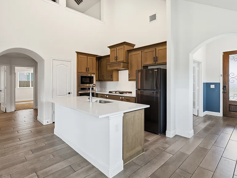Open concept kitchen featuring an island with a built-in sink, stainless steel appliances, wood-finish cabinetry, and light-toned countertops