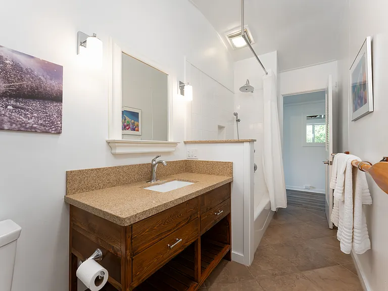 Updated main bathroom featuring stone countertops, custom wood vanity, and tub/shower combination.