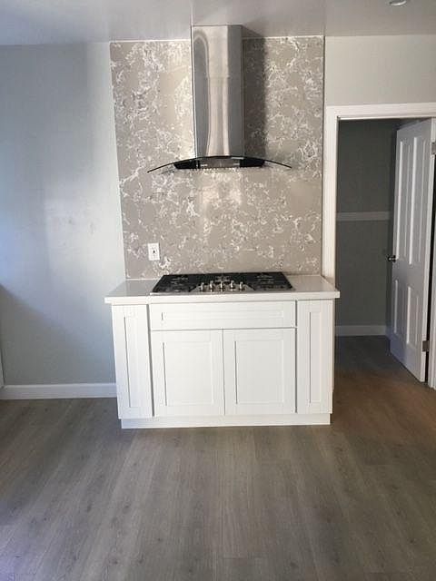Gas cooktop with five burners and direct outside vent hood. Doorway leading to back entrance and pantry.