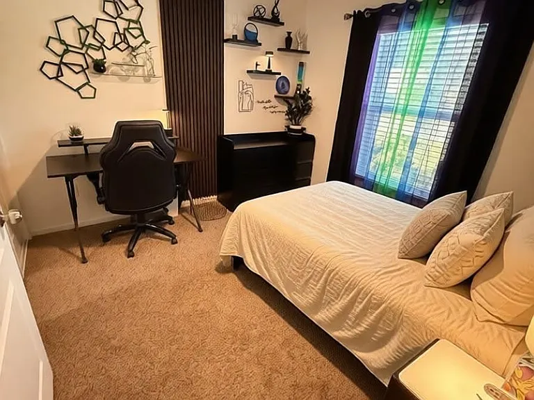 Furnished bedroom with full bed, nightstand, and a dedicated desk setup, plus a window with blinds and ceiling fan.