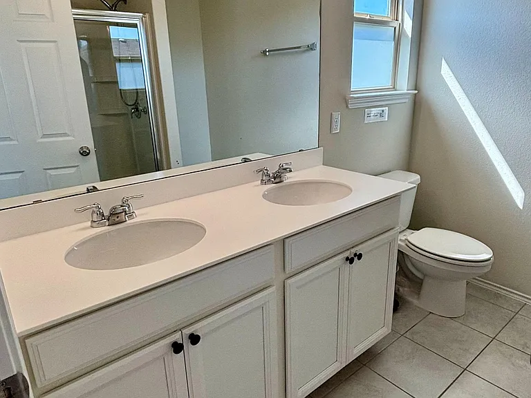 Bathroom with double-sink vanity, large mirror, tile flooring, and a window for natural light; shower/tub combo nearby.