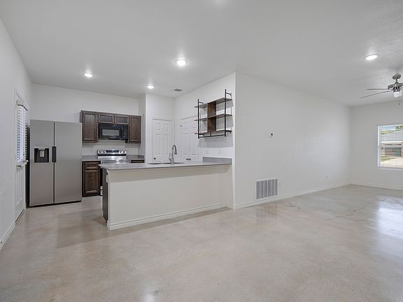 Open-concept layout combining the kitchen, dining area, and living room. Features polished concrete floors, recessed lighting, and a breakfast bar overlooking the main living space.