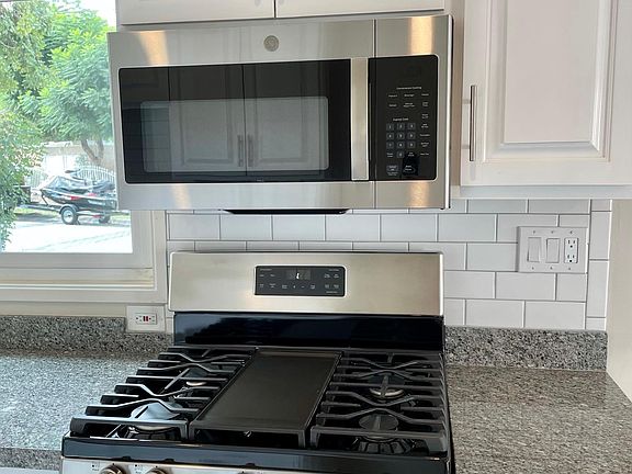 Six burner gas stove with microwave range above. Kitchen is vented.