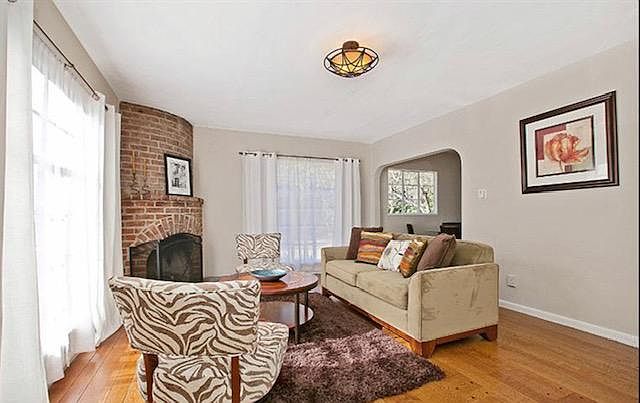 Living room with unique round corner fireplace and mantle. Large windows with ample bright light.