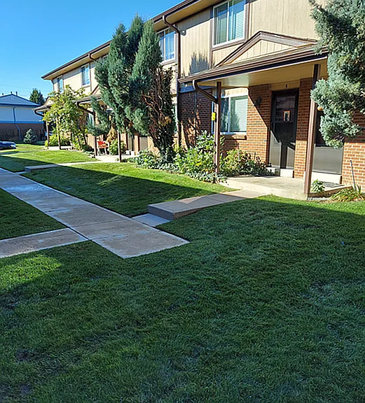 Charming townhouse exterior with lush green lawns, pathway, and welcoming porch, perfect for comfortable living.