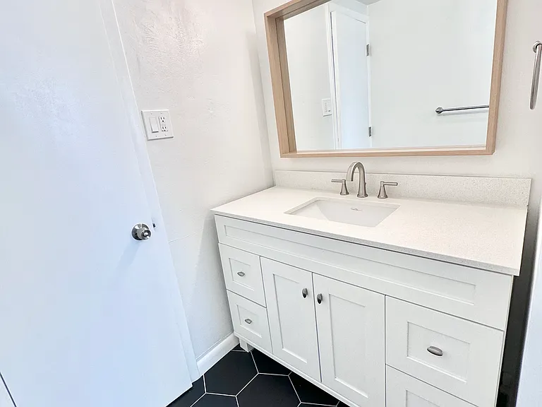 Modern bathroom with sleek white vanity, large mirror, and stylish hexagonal black tiles. Modern bathroom with sleek white vanity, large mirror, and stylish hexagonal black tiles.