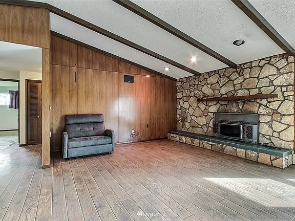 View one of large family room with cathedral ceilings, exposed beams, nice flooring and wood stone fireplace. 