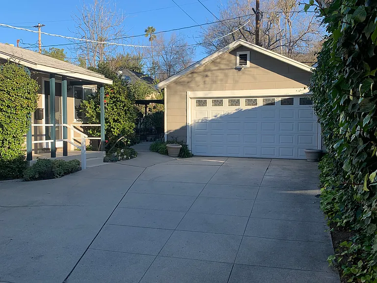 Small cottage house on the left and pathway to back yard between the house and the garage.