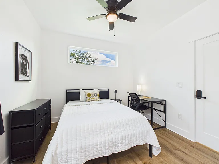 Furnished bedroom with a ceiling fan, dresser storage, and a dedicated desk area, plus a high window for natural light.