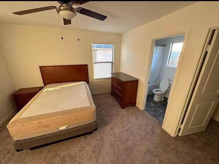 Furnished bedroom with ceiling fan, window blinds, and dresser storage, plus convenient access to an en-suite bath.