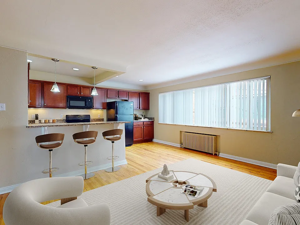 Charming open-plan living room with elegant hardwood floors, featuring a cozy seating area and a modern bar-style kitchen with warm wooden cabinetry.