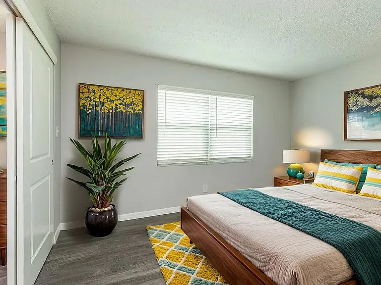Bright and inviting bedroom with modern decor, featuring a cozy bed with colorful cushions, vibrant artwork, and a large potted plant for a touch of greenery.