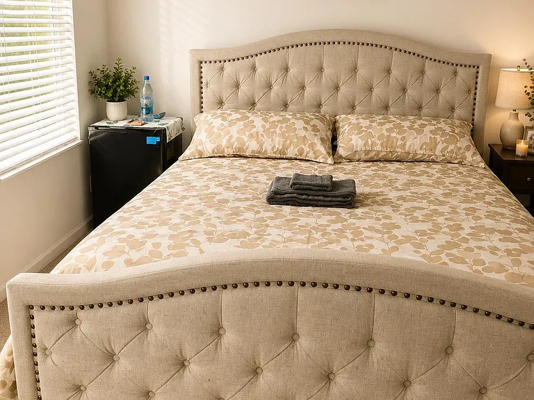 Well-appointed bedroom with a tufted bed, bedside lighting, and a window with blinds for natural light and privacy.