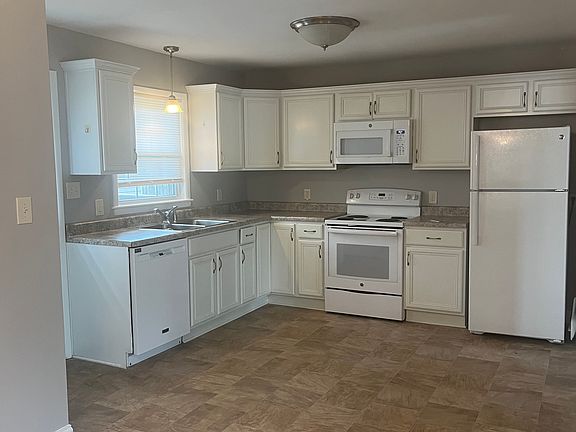 Eat in kitchen with new dishwasher, microwave and refrigerator. White cabinets and pantry in hall