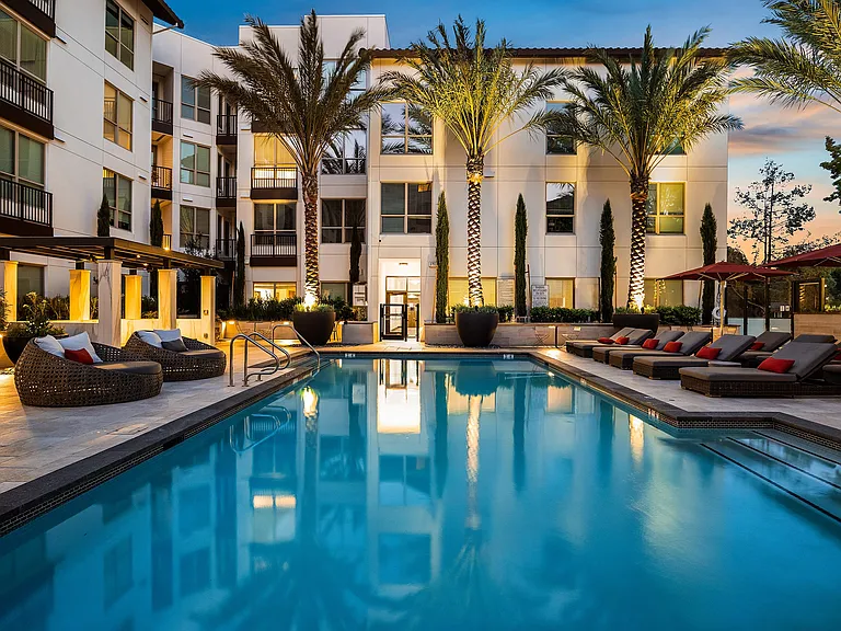 Twilight poolside with glowing water, landscaping, and seating