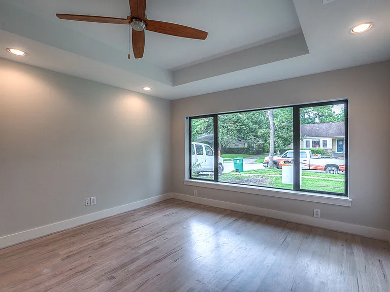 Light-filled study/bedroom with tray ceiling, designer ceiling fan, and a large picture window framing the front-yard view