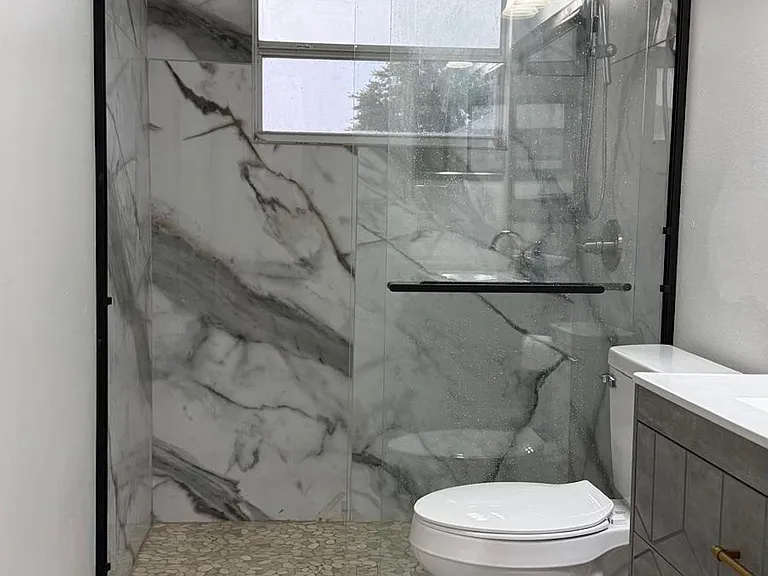 Updated bathroom with a glass-enclosed shower, large-format tile surround, and vanity storage with a sleek countertop.