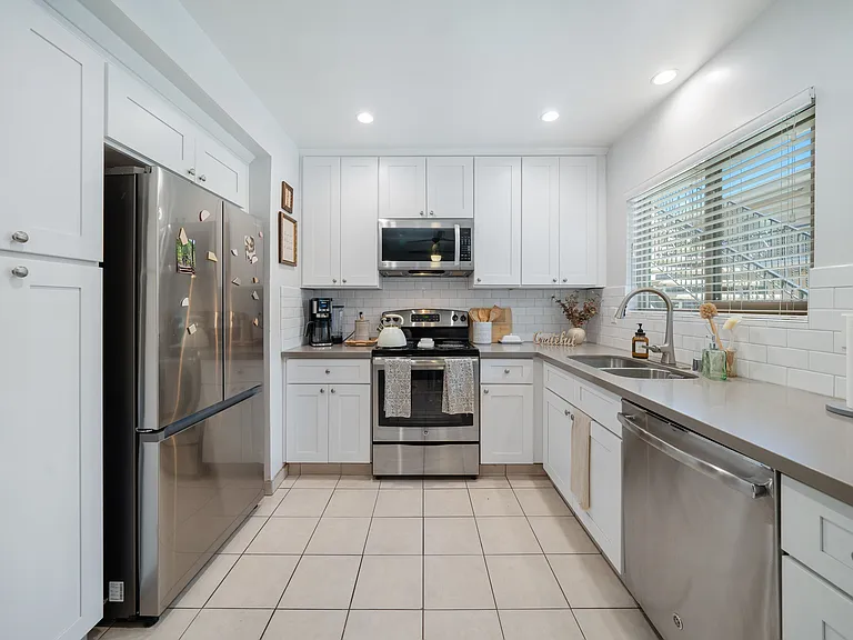 #12 Kitchen- stainless steel electric stove, dishwasher & microwave. Gray quartz countertop, white cabinetry Recessed ceiling lights & tile floor.
Horizontal blinds