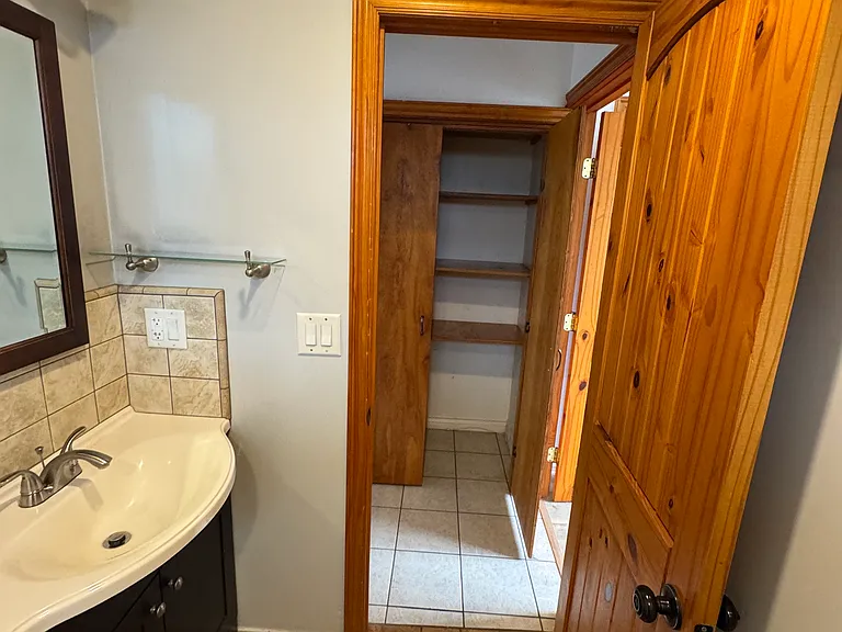 Bathroom showing closet in the hallway, porcelain tiles in the bathroom. Two panel pine solid wood clear stain bathroom door.