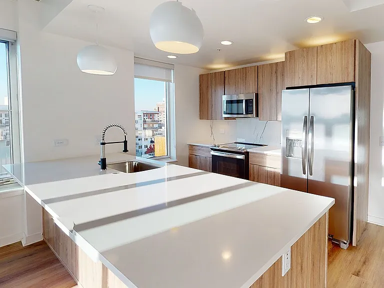 Apartment kitchen with stainless steel appliances, quartz countertops and wood-style flooring.