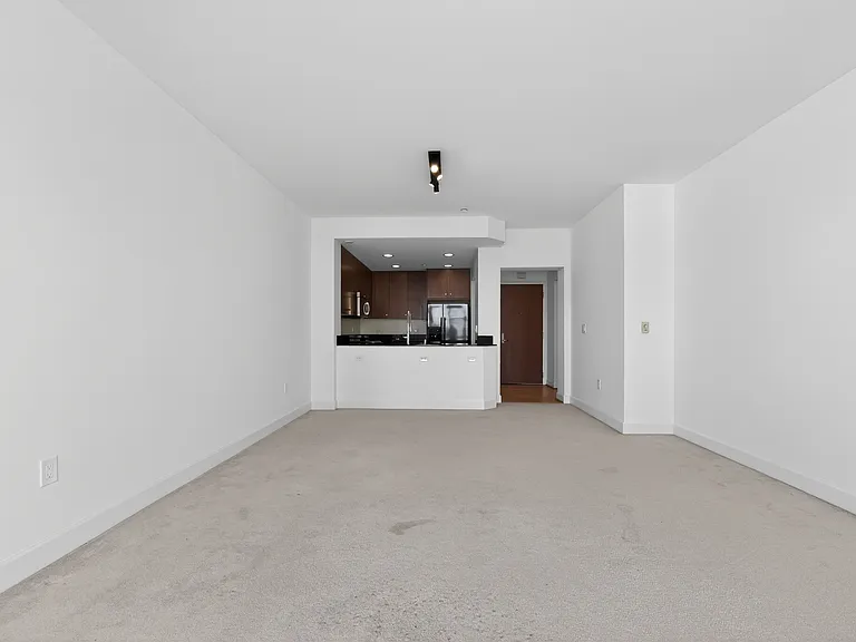 Spacious living room with high ceilings, updated lighting, recently painted white walls, and open sightline to the kitchen, entryway, and front door.