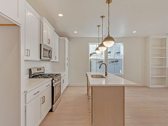 Modern kitchen with white cabinets, stainless steel appliances, a center island with a sink, pendant
