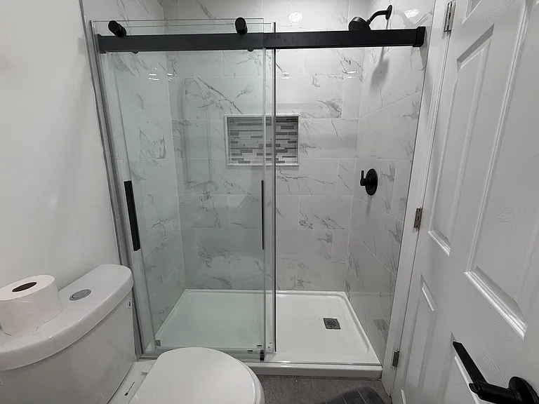 Walk-in shower with frameless glass doors, marble-look tile surround, and matte black fixtures for easy daily use.