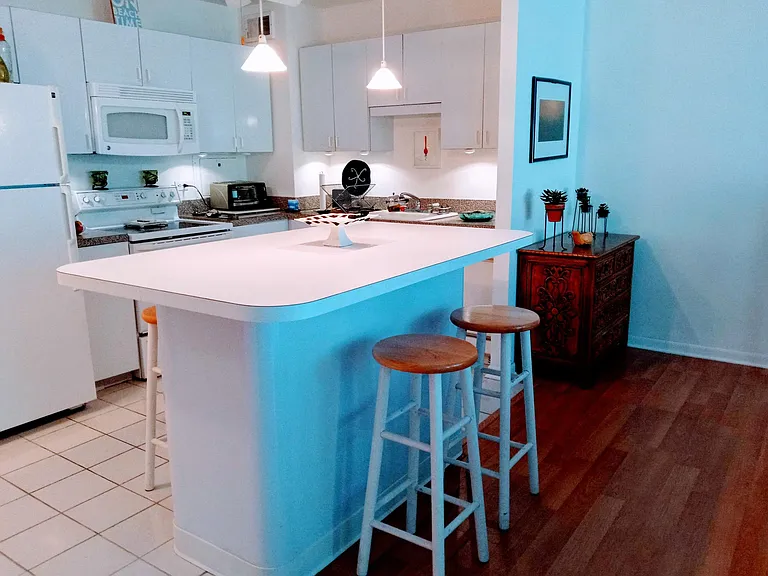 Italian kitchen with lights below cabinets. White tile floor in kitchen. Ample storage in island and cabinets. Built-in dishwasher, electric stove/oven, microwave and fridge.