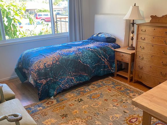 Spacious bedroom with adult size twin bed, nightstand, chair with ottoman, high it dresser and roomy closet
