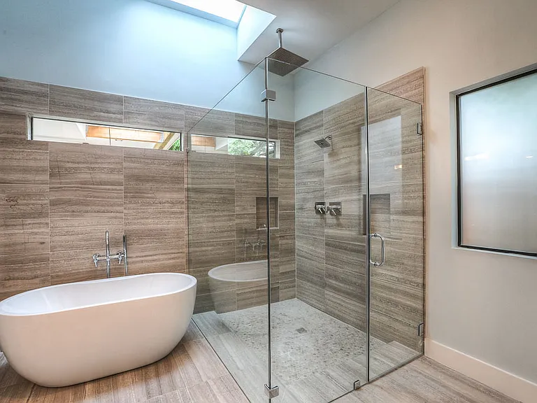 Spa-style master bath with freestanding soaking tub, oversized walk-in shower with frameless glass, natural marble tile, transom windows, and an overhead skylight