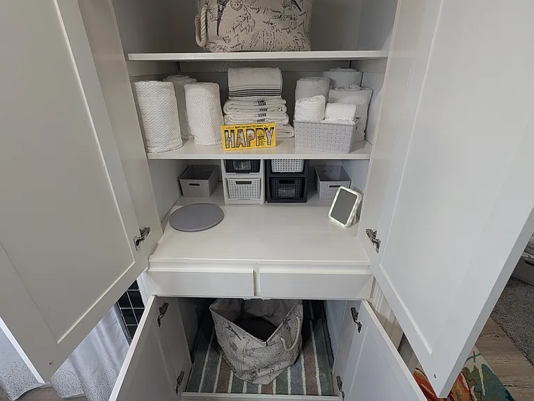 Bathroom storage galore! The space features shelving for linens and a towel area. Empty cubbies and a convenient Lazy Susan help organize personal items. A hamper is provided for laundry. No drawers here, but there are two drawers in the bathroom vanity.