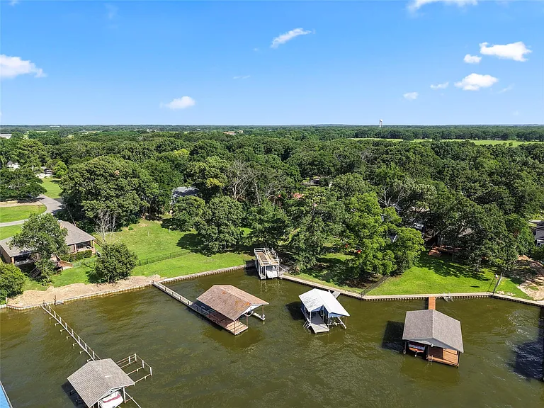 Waterfront property featuring multiple boat docks, mature trees, and a clear blue sky