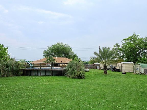 Now we're looking at the Back of the Home with a custom built deck surrounding an above ground pool. Also to the right are several storage sheds.