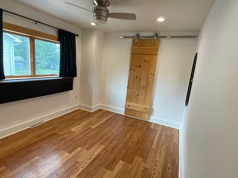 Bright primary bedroom with hardwood floors, ceiling fan, and charming wood barn door detail.