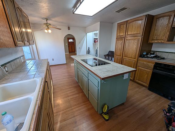 Kitchen with newly refurbished cabinets and counter tile grouting and resealed ,kitchen island with built in electric 4 burner glass cook top, built in gas oven to the right under microwave shelf.