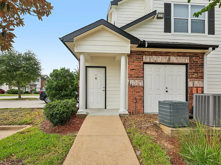 Inviting townhouse-style apartment entrance with classic brick and white siding, manicured shrubs, and a sleek modern pathway. Inviting townhouse-style apartment entrance with classic brick and white siding, manicured shrubs, and a sleek modern pathway.