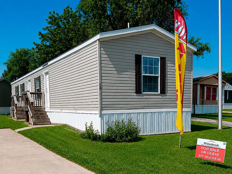 Exterior view of the manufactured home at Winterbrook Lot 349 in Greenwood, Indiana. Features blue siding, a welcoming entry with wooden steps and railings, and a well-maintained lawn within the Winterbrook community.