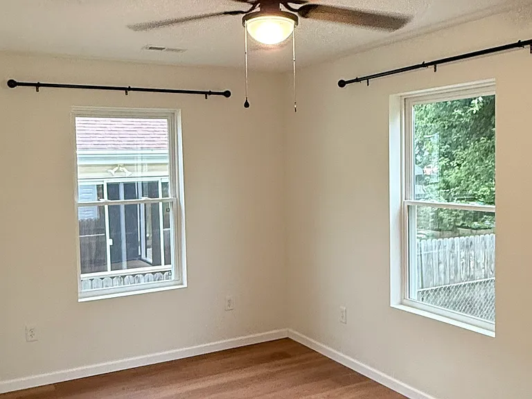 Spacious bedroom featuring two windows with installed curtain rods for plenty of natural light, a ceiling fan with light, attractive flooring, and a large walk-in closet with built-in shelving for generous storage.