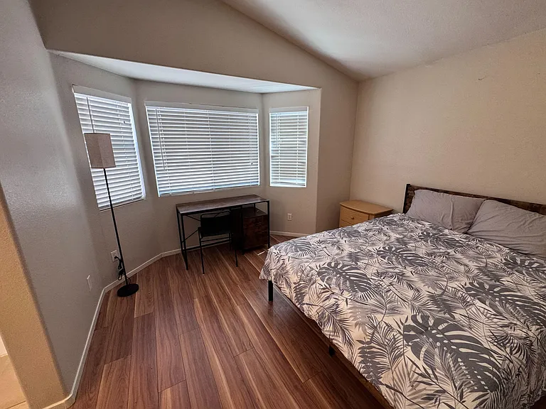 Furnished bedroom with wood-look flooring, a full bed, nightstand, and a dedicated desk area by the window.
