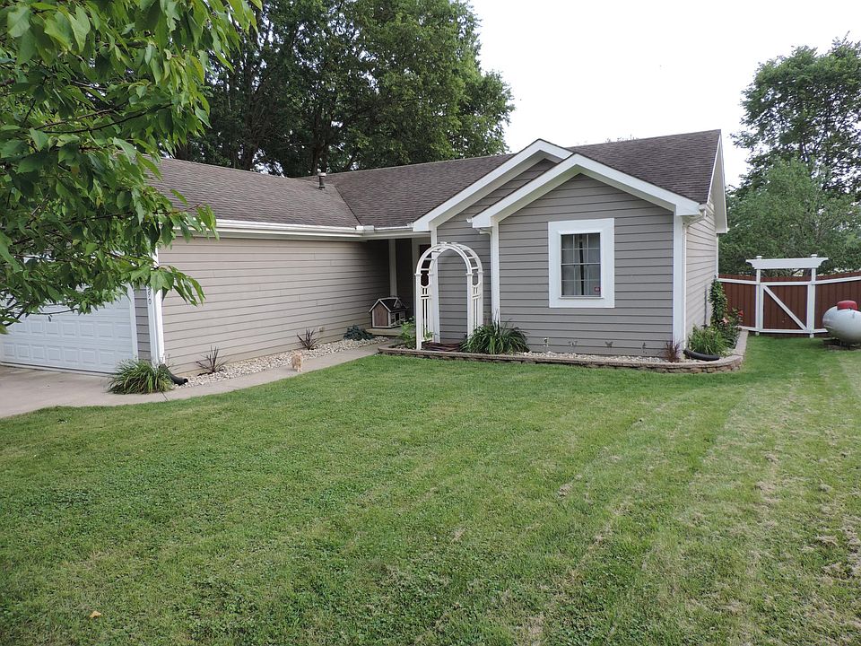 Front of the house; river rock flower beds bordering the house, with day lilies and a clematis plant. Cherry, plum, and peach trees are in the front yard.