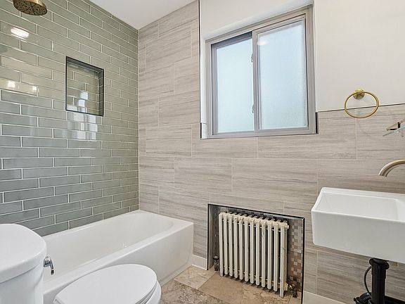 Modern bathroom with elegant green subway tiles, a sleek white bathtub, and a stylish sink under a bright window.