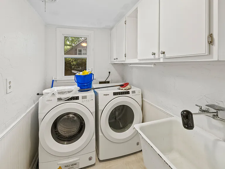 Convenient laundry room with front-load washer & dryer, utility sink, upper cabinet storage, and natural light.