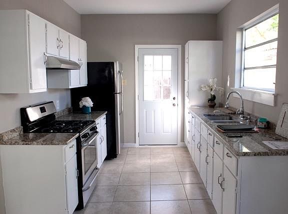 Kitchen features stainless steel refrigerator, gas range/oven, & hood fan and light, granite countertops, tile floors, and ample cabinetry for storage.