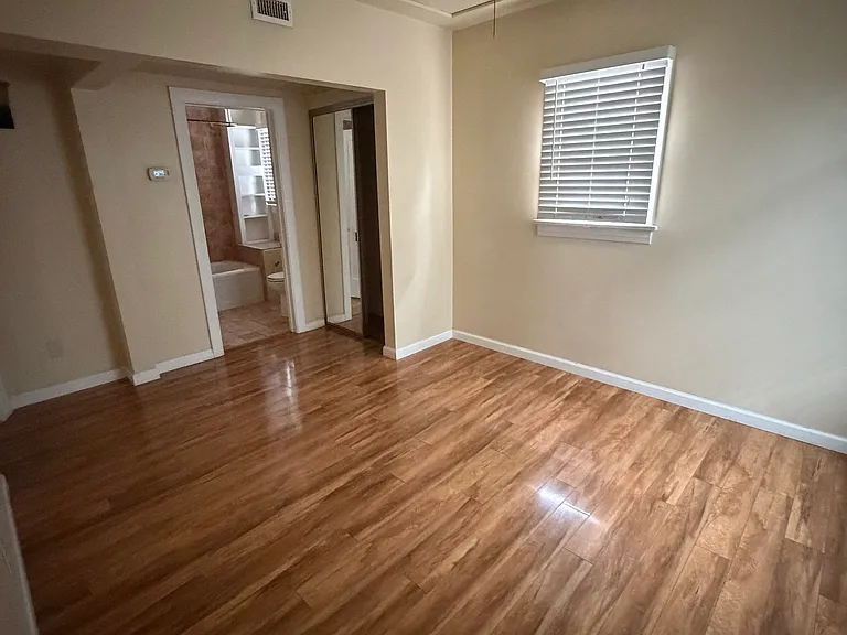 Room for rent, looking Northeast towards back of house & side patio. Private bath visible thru doorway, thermostat for entire house on the wall. New blinds installed & shelves hung in closet.