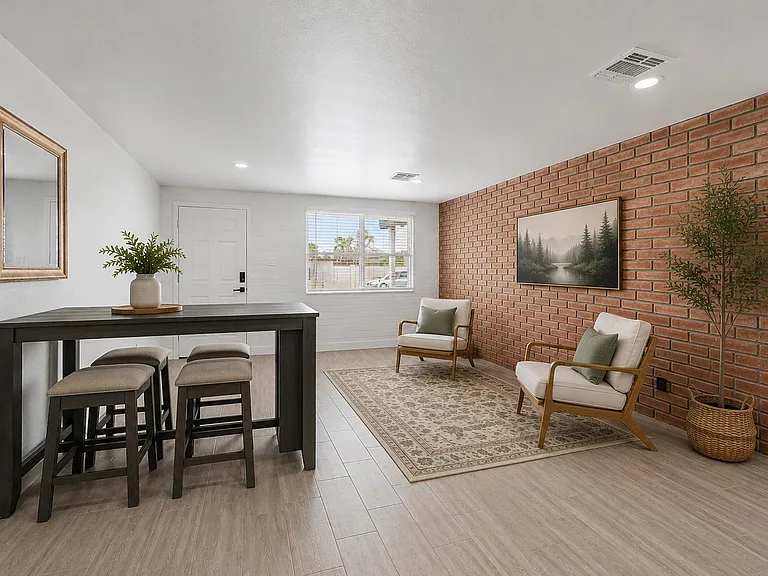 Open common area with brick accent wall, lounge seating, and a bar-height table near the entry and window.