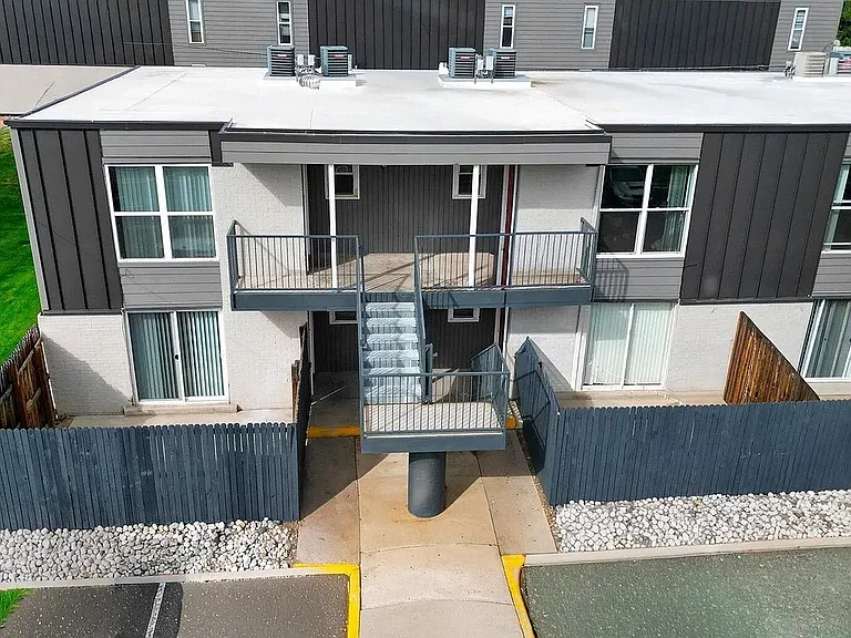 Modern apartment exterior featuring sleek design with balcony, surrounded by well-maintained greenery and secure fencing.