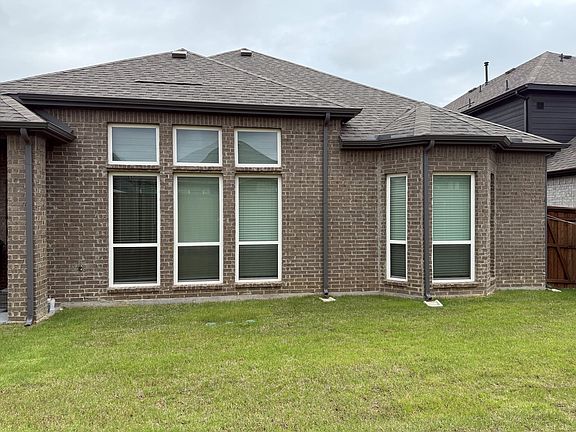 Brick exterior with a gabled roofline, multiple white-framed windows, dark gutters, and a grassy lawn