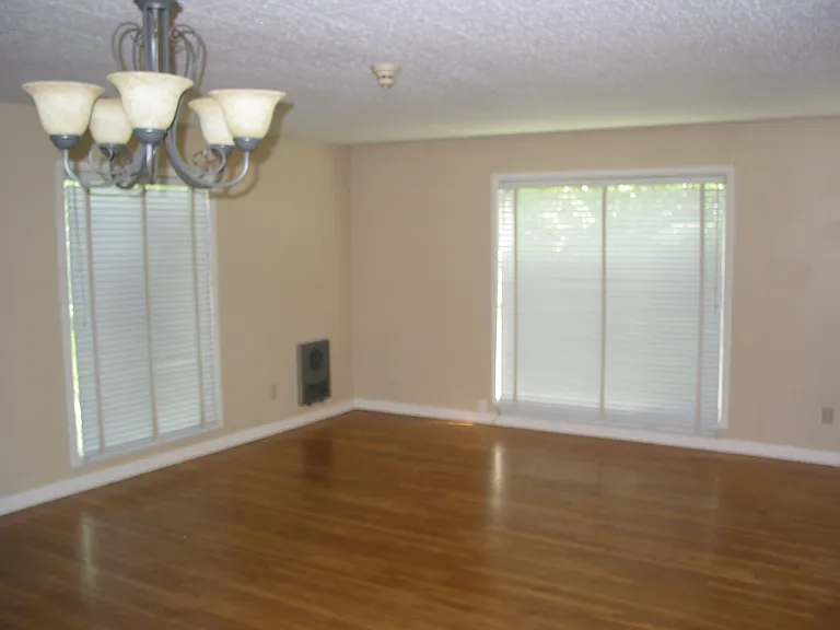 Living room with hardwood floors, floor-to-ceiling windows (shades closed).